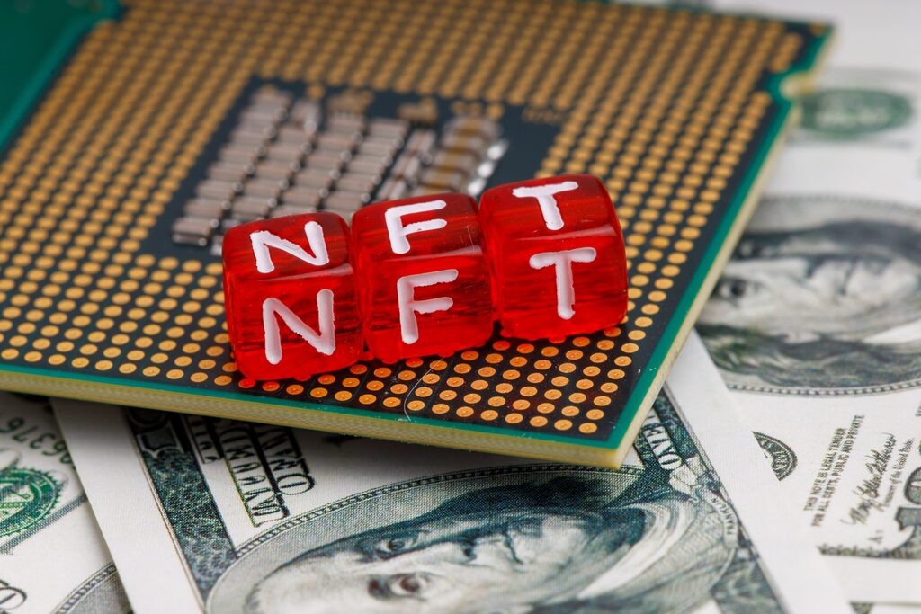 Three red dices spelling "NFT" are put together on a computer part on a pile of cash.