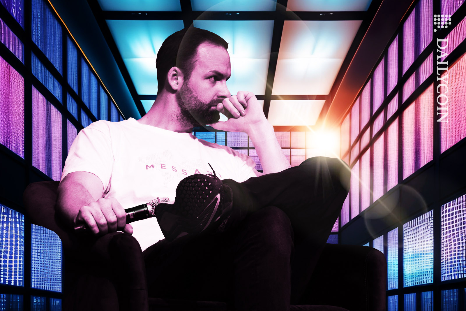 Messari CEO Ryan Selkis thoughtful sitting in a chair in a room surrounded by purple windows while holding a microphone.