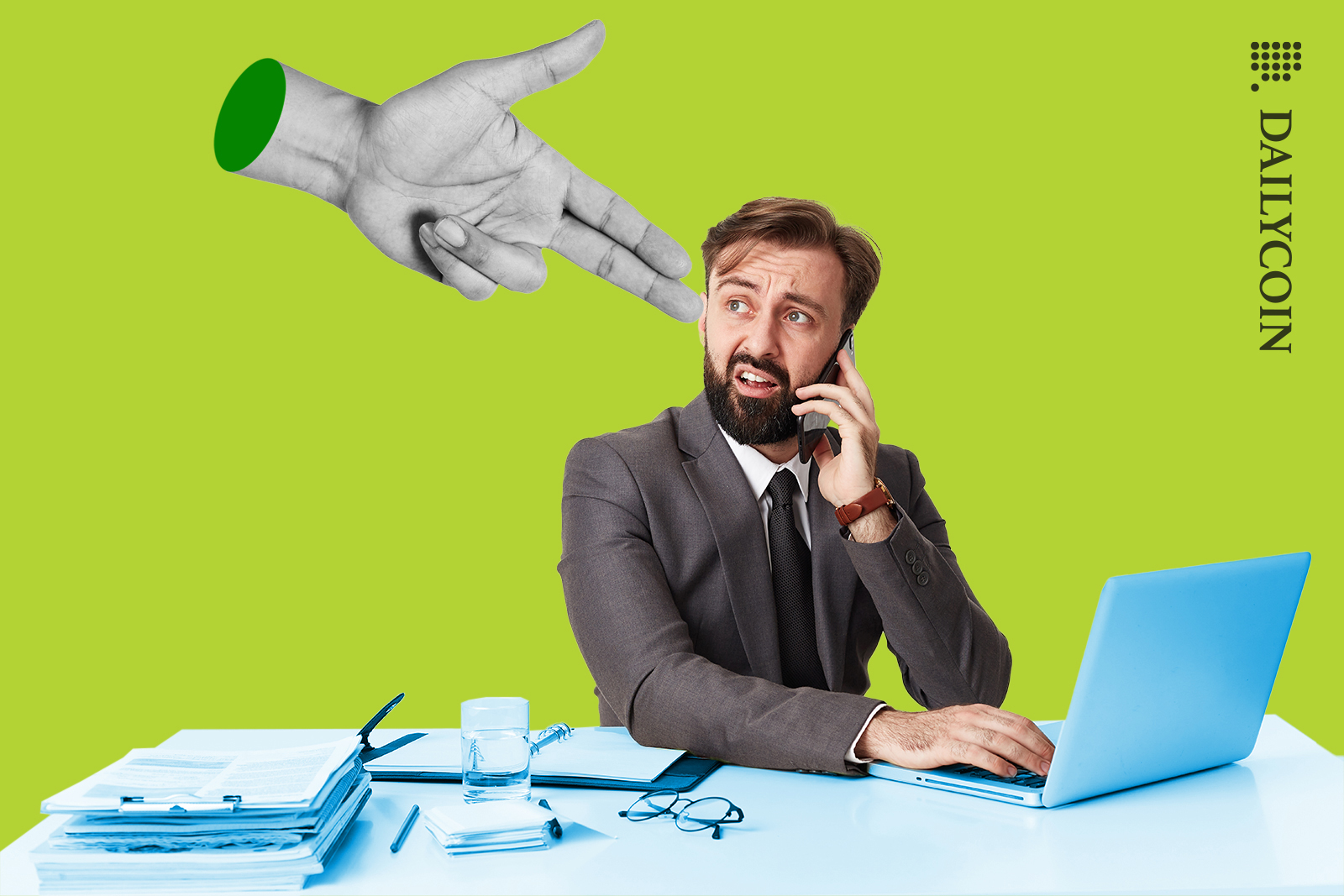 Man on the phone sitting at a desk with his laptop. Gun fingers pointing to his head.