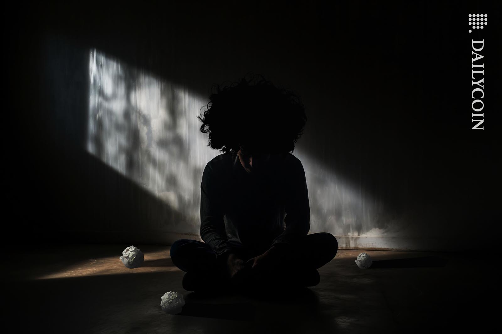 Sam Bankman Fried sitting in a dark prison cell surrounded by crumbled paper balls.