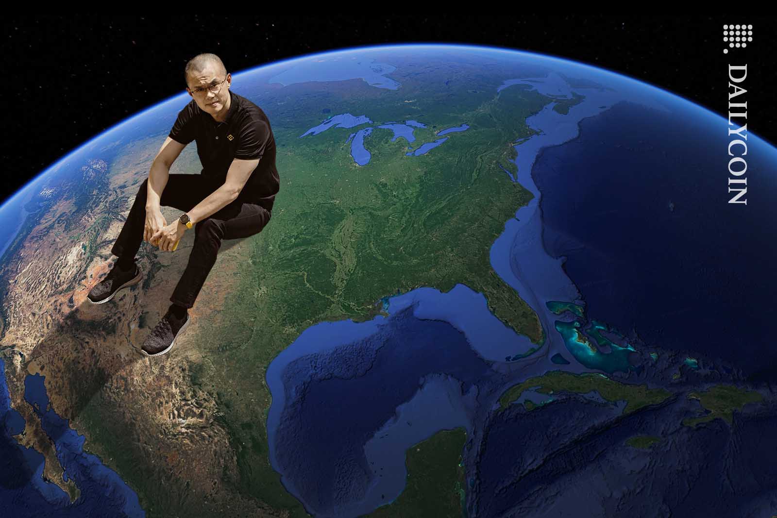 Changpeng Zhao sitting on planet earth, looking up to the camera.
