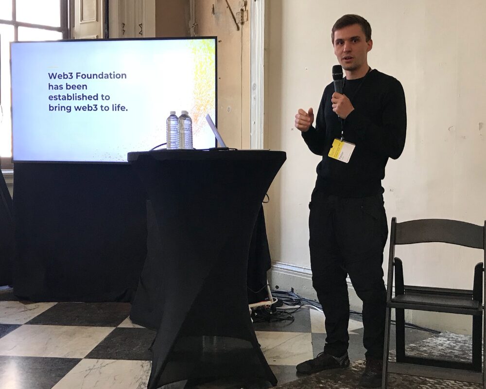 Peter Czaban speaking at a conference with a presentation in the back which says "Web3 Foundation has been established to bring Web3 to life".