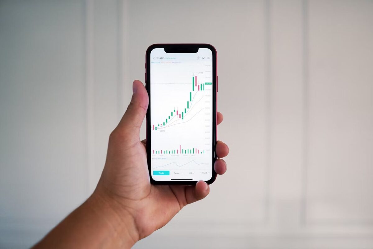 A man holding a phone with open trading stocks app.