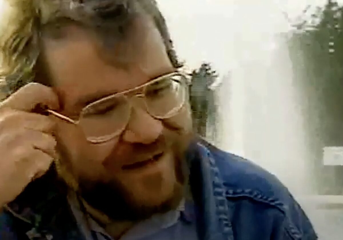 Phil Zimmermann with a confused look on his face as he adjusts his glasses. A water fountain is behind him.