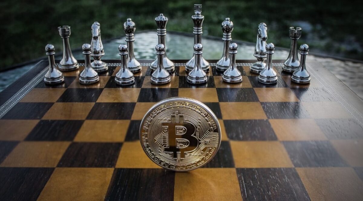 Bitcoin token with numerous chess pieces behind it on a chess board.