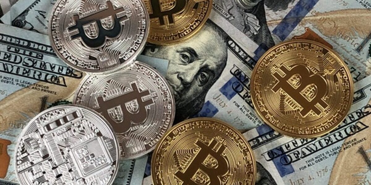 US dollar bill being covered with Bitcoin tokens scattered around it.