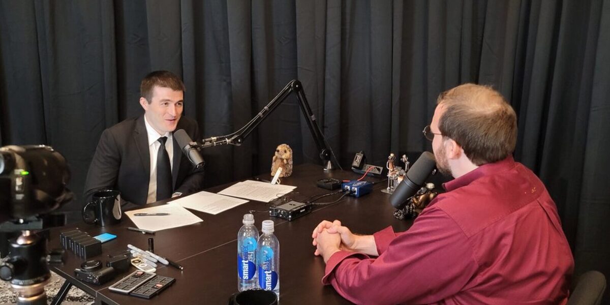 Lex Fridman sitting across a desk from Cardano founder, Charles Hoskinson.