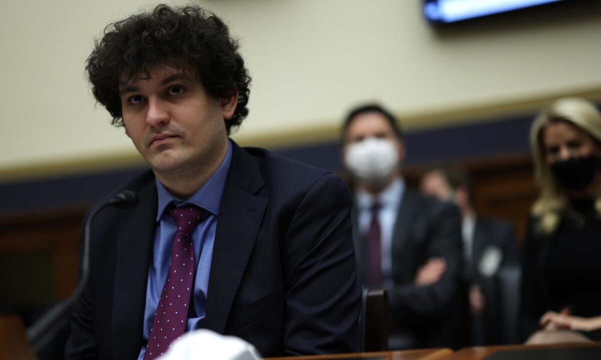 Sam Bankman-Fried with a guilty look on his face sitting in a courtroom with a man and woman sat behind him with masks on.