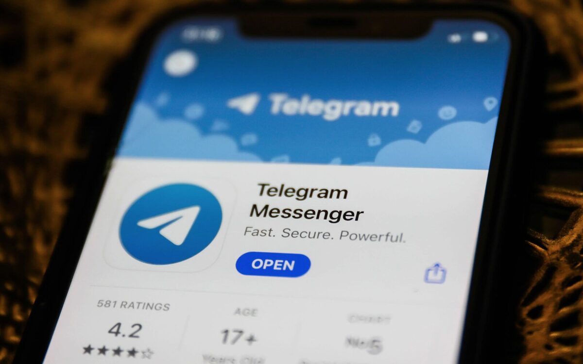 A phone screen with the Telegram Messenger logo on the front. Underneath is an 'Open' button in blue.