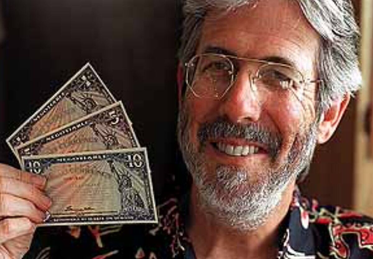 Bernard Von NotHaus holding up three Liberty Dollar bills with a smile on his face.