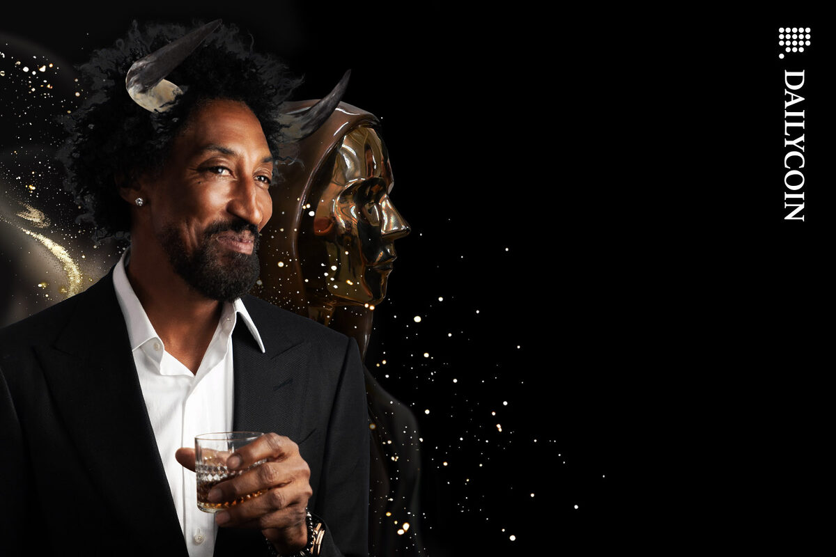Scottie Pippen with horns holding a drink, posing with a Satoshi statue.