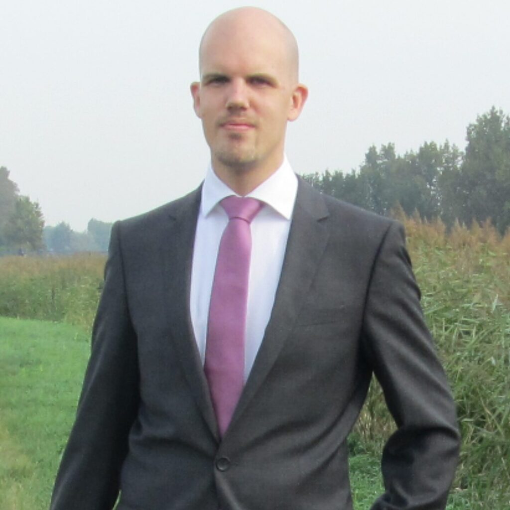 Patrick Lodder standing in a field wearing a black suit and red tie.