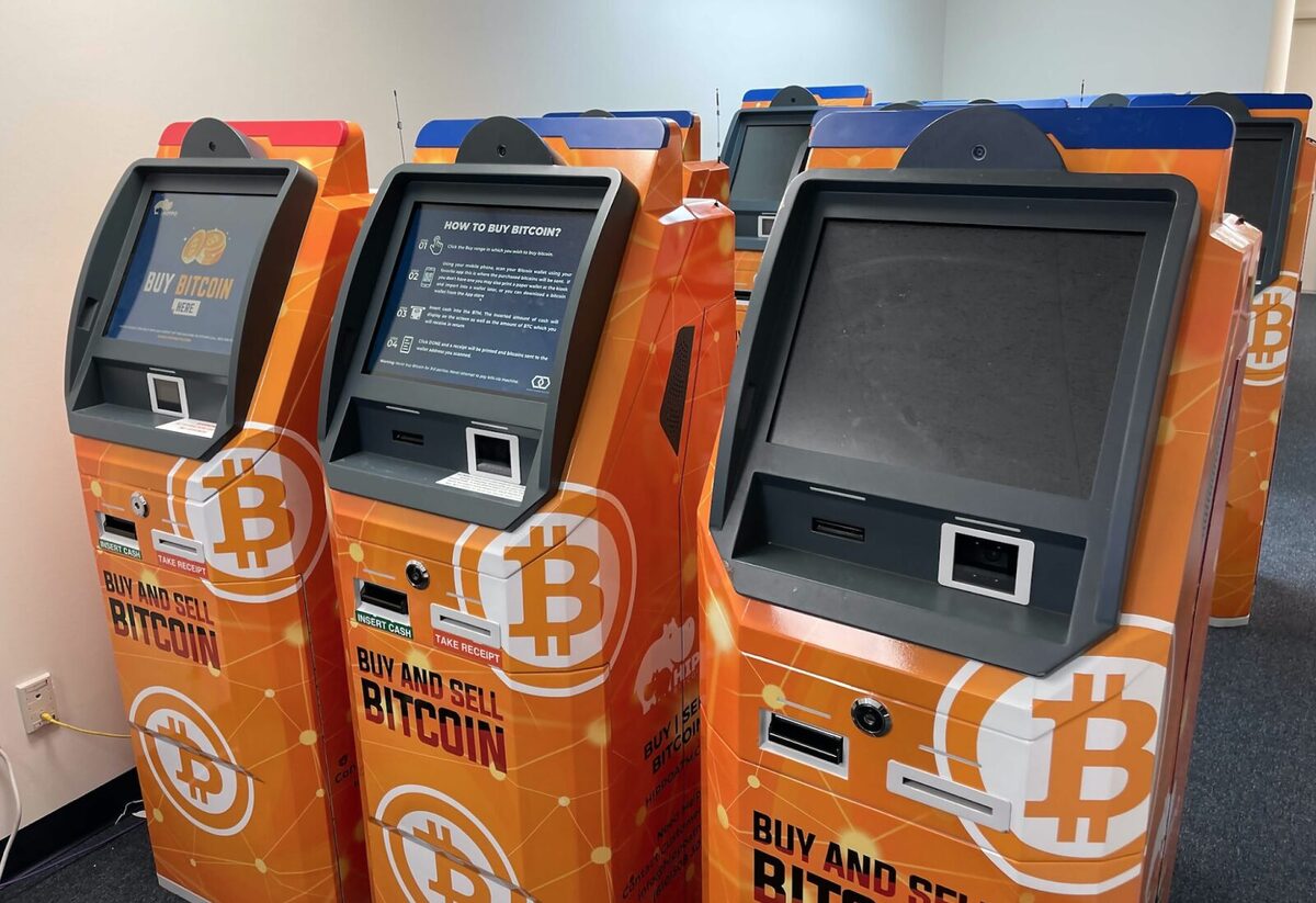 Three orange Bitcoin ATMs next to one another. Two have their screens on, and the one on the furthest right doesn't.