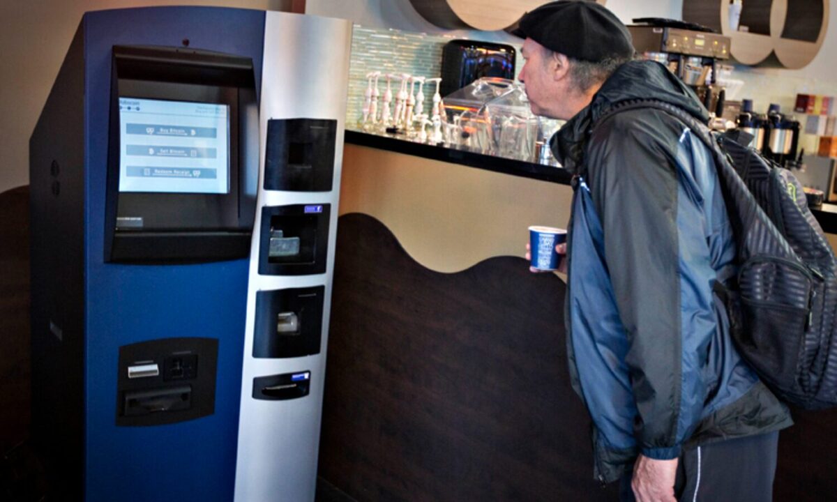 A man in a blue and black jacket staring at the first crypto ATM in a coffee shop with a bewildered look on his face.