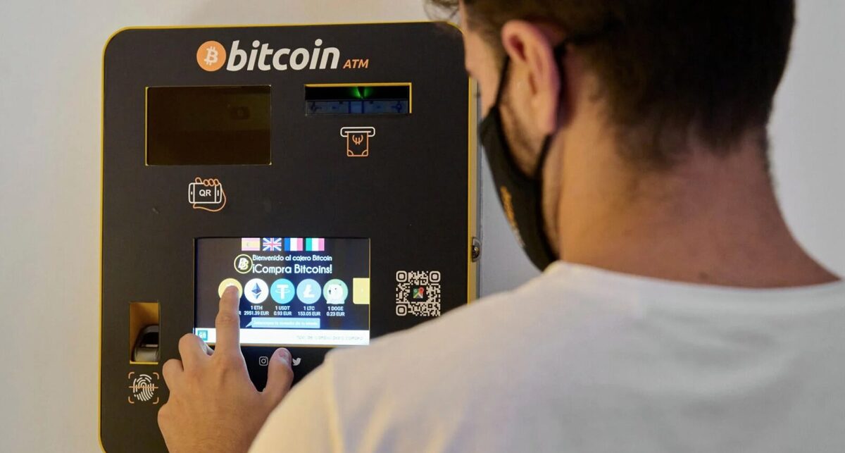A man choosing a token on a crypto ATM. On the screen can be shown Bitcoin, Ethereum, Litecoin and Dogecoin.