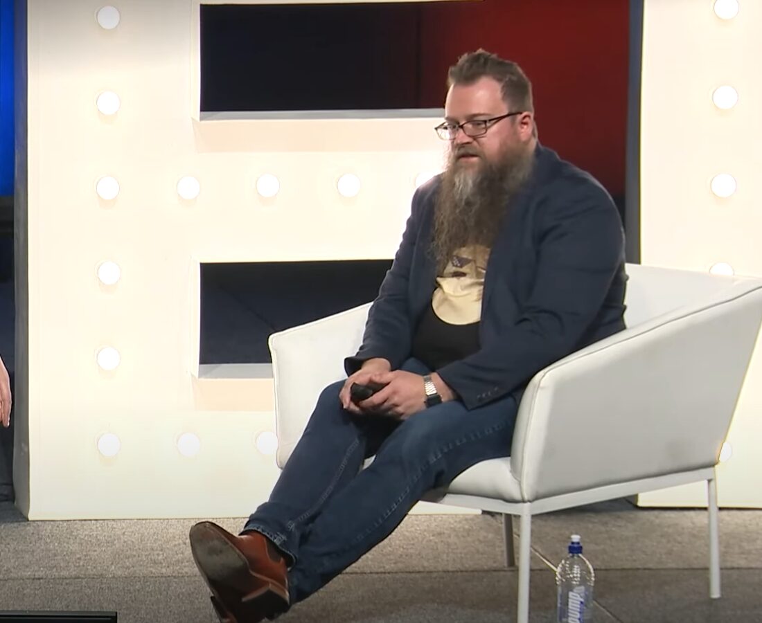Timothy Stebbing sitting on a white chair at a Dogecoin conference.