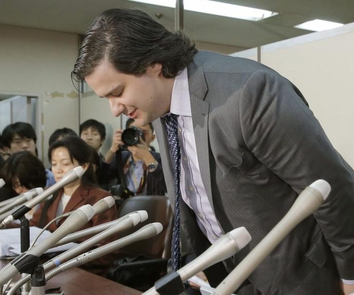 Mark Karpeles bowing while standing up in a conference room surrounded with onlookers.
