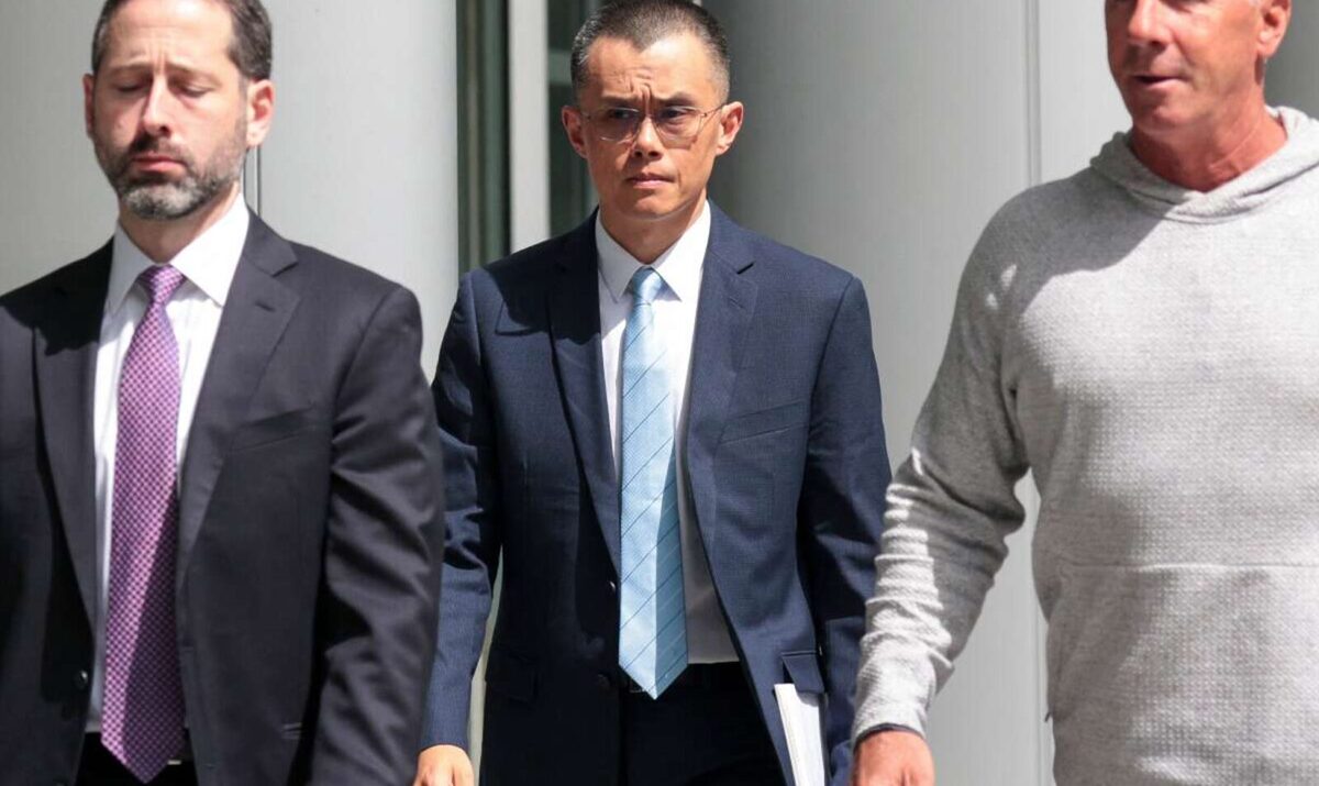 Changpeng Zhao being escorted by a lawyer and security guard. Zhao has a concerned look on his face.