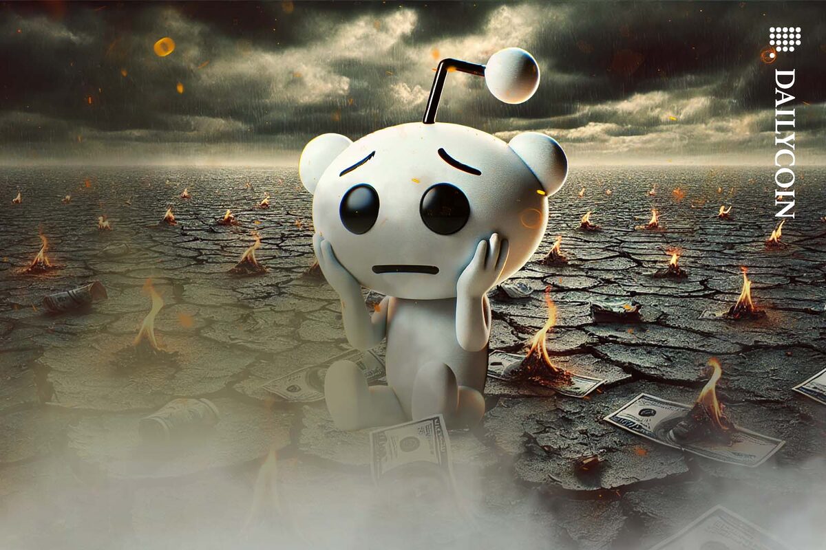 The Reddit mascot holding its had in sadness as its sitting in a landscape with burning banknotes scattered around.